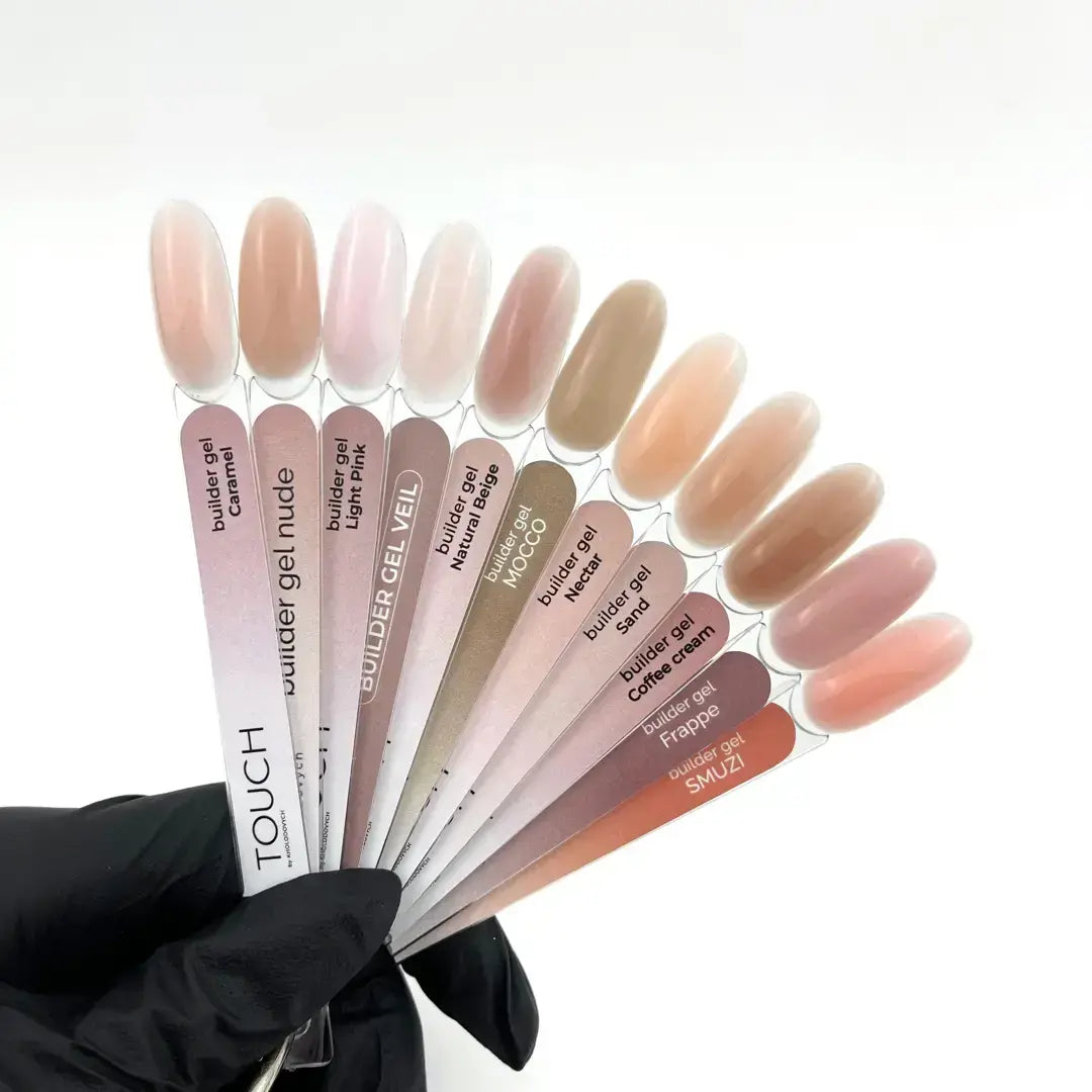A hand wearing a black glove holds a fan of nail polish sample sticks with almond-shaped nail tips showing various nude, beige, pink, and brown shades. The sample sticks are labeled with shades such as Caramel, Light Pink, Beige, and Coffee Cream.